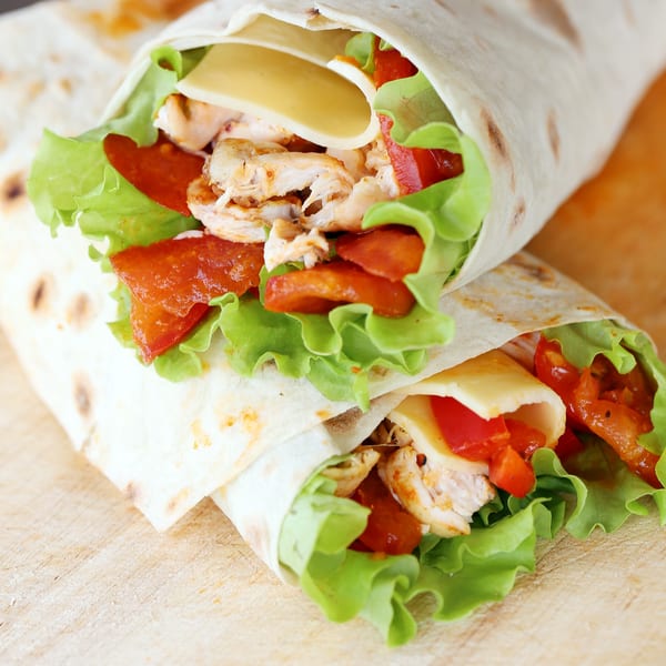 Two chicken and vegetable wraps with cheese and red sauce on a wooden surface.