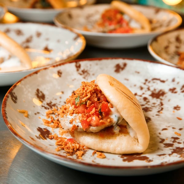LA Tacos & Kabobs' bao bun with chicken, white sauce, diced tomatoes, and crispy fried onions.