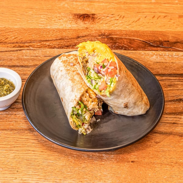 Two large, cut burritos filled with meat, rice, lettuce, and tomatoes, served with green salsa.