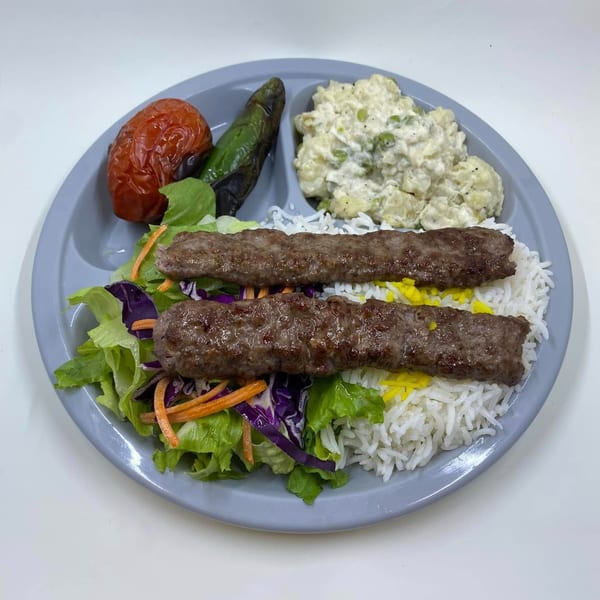 Two kabobs on a bed of rice with salad, roasted tomato, pepper, and potato salad.