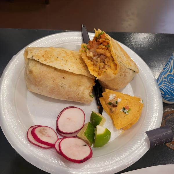 Two LA Tacos & Kabobs burritos, one cut open, with radishes, lime wedges, and a tortilla chip.
