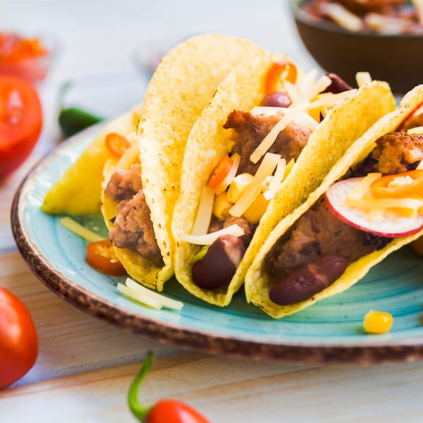 Close-up of three LA Tacos & Kabobs hard-shell tacos filled with meat, cheese, and vegetables.