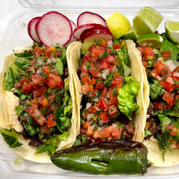 Three LA Tacos & Kabobs tacos with meat, lettuce, pico de gallo, radishes, limes, and a charred pepper.