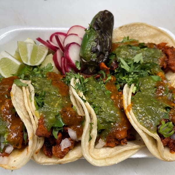 Four LA Tacos & Kabobs tacos with green and red salsa, cilantro, limes, radishes, and a grilled jalapeño.